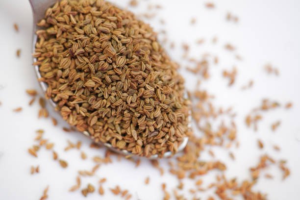 Ajwain seeds in a spoon over white background. Selective focus.